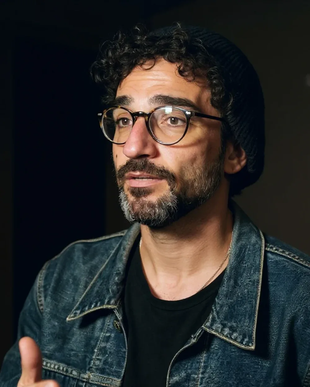 Un hombre de unos treinta y cinco años con gorro de lana, gafas redondas de carey y cazadora vaquera, hablando a cámara entre bastidores.