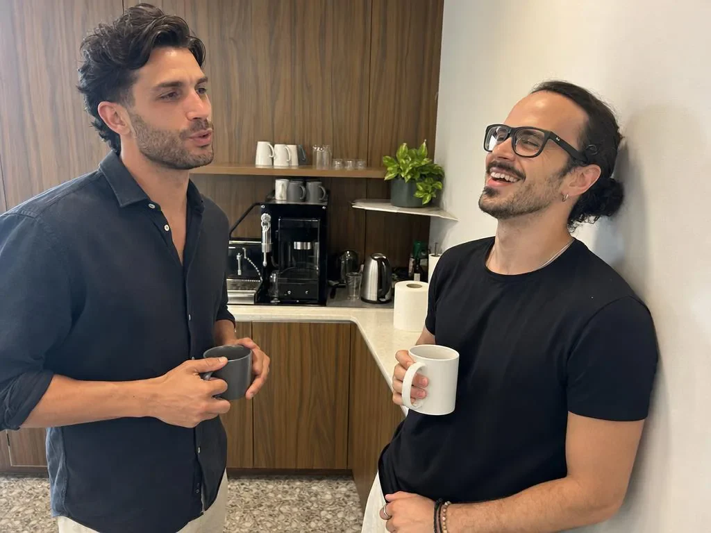 Los dos fundadores charlando de pie con sendas tazas en el rincón de café de la oficina.