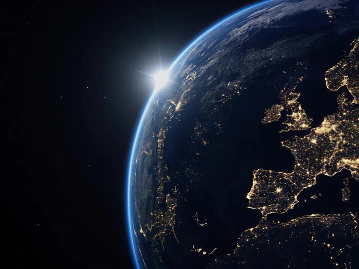 La Tierra vista desde el espacio de noche, con Europa iluminada y el sol asomando por el borde del planeta.
